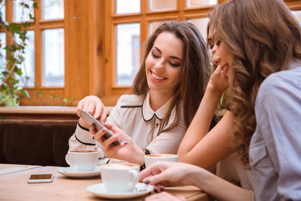 Three people smiling and using smartphone in cafe together